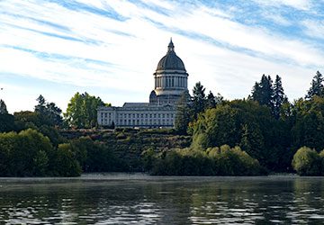 view of the capitol building surrounded by trees in Olympia, Washington from the water