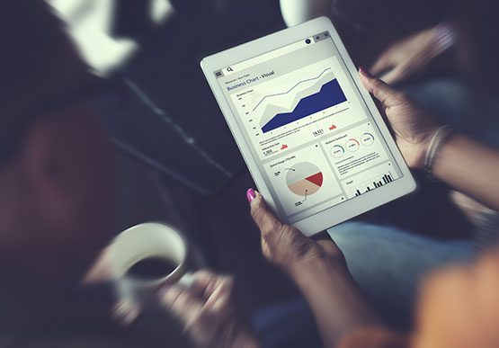 woman holding an ipad looking at analytics information and graphs surrounded by two other people looking at the data