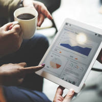 woman holding an ipad looking at analytics information and graphs surrounded by two other people looking at the data