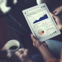 woman holding an ipad looking at analytics information and graphs surrounded by two other people looking at the data